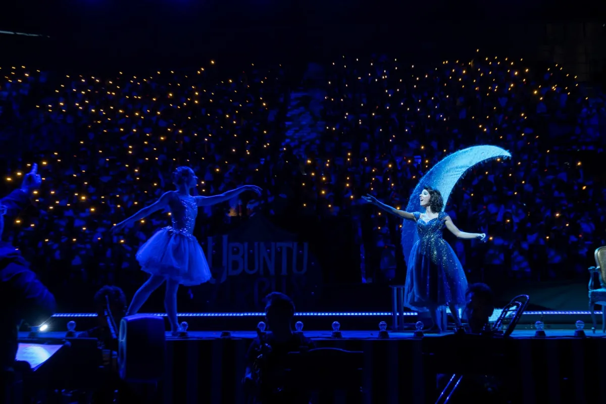 Proyecto Ubuntu — escena con bailarinas y luna creciente ante miles de luces del público